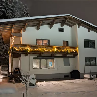 Ein modernes Haus im Schnee, beleuchtet mit Lichtern. Die Umgebung ist winterlich und friedlich.