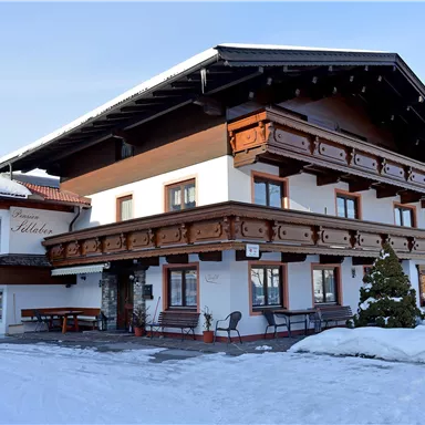 A traditional house in alpine style, surrounded by snow. The facade is adorned with wooden decorations and a balcony.
