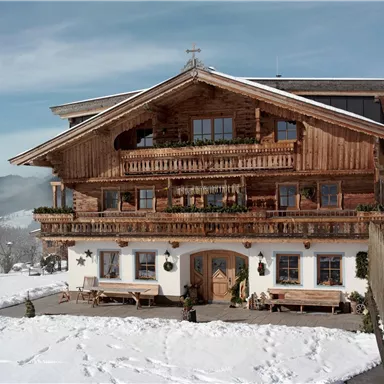 Ein traditionelles Chalet aus Holz in einer schneebedeckten Landschaft. Die Berge sind im Hintergrund sichtbar und der Himmel ist klar.