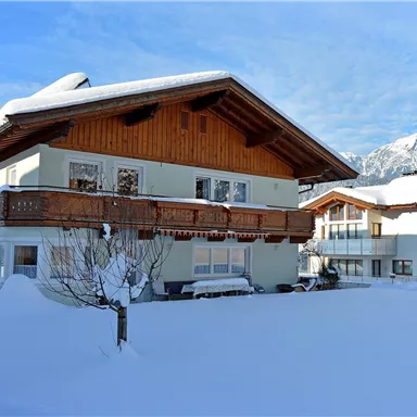 Ein wunderschönes Haus im Schnee mit einem großen Balkon. Im Hintergrund sind schneebedeckte Berge zu sehen.