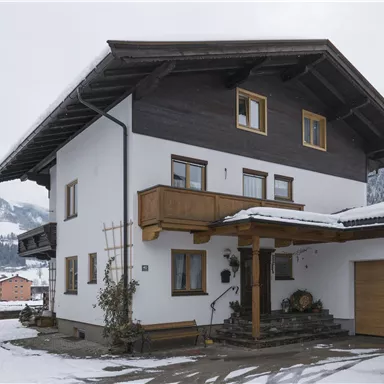 Ein schönes Haus in den Alpen, umgeben von schneebedeckten Bergen. Die Fassade ist weiß mit einem Holzbalkon.