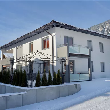 Ein modernes Haus mit zwei Etagen, umgeben von Schnee. Im Hintergrund sind Berge zu sehen, und das Gebäude hat einen klaren, eleganten Stil.