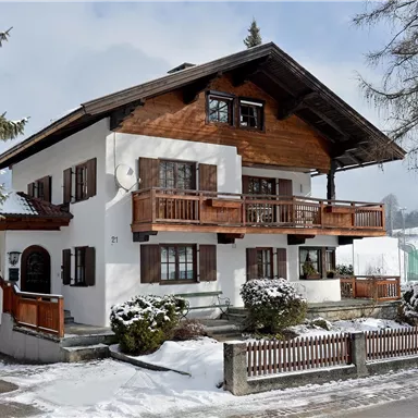 A charming house in alpine style, surrounded by snow and trees. The balcony and wooden cladding give it a cozy atmosphere.