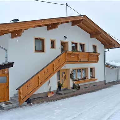 Ein gemütliches Haus im Schnee mit einem Holzbalcony. Die Umgebung ist winterlich und ruhig.