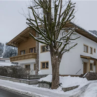 Ein modernes Haus in einer winterlichen Landschaft, umgeben von Schnee. Bäume und Berge sind im Hintergrund sichtbar.