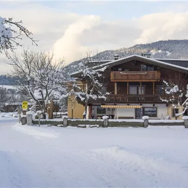 Ein gemütliches Haus im Schnee, umgeben von einer winterlichen Landschaft. Die Bäume sind mit Schnee bedeckt und die Atmosphäre ist ruhig und friedlich.