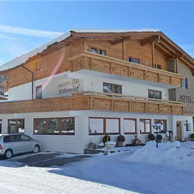 A charming hotel with traditional wooden architecture, surrounded by snow-covered mountains. Guests have access to parking in front of the building.
