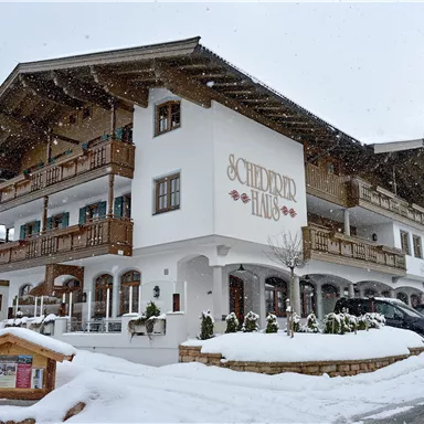 A picturesque hotel in the winter snow with traditional alpine architecture. The entrance is surrounded by beautiful greenery and winter decorations.