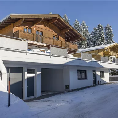 A rustic wooden house in the snow with a blue sky in the background. Surrounded by snow-covered trees and other chalets.