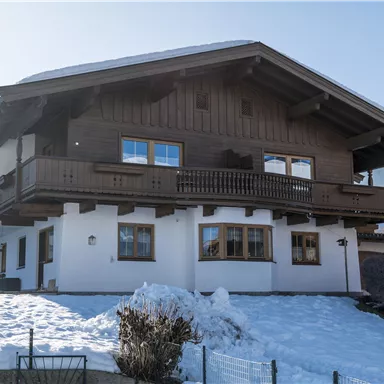 Ein gemütliches Haus im Alpenstil mit Holzverkleidung. Der Schnee bedeckt den Boden und die Umgebung ist bergig.
