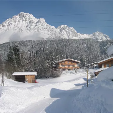 Eine verschneite Landschaft mit beeindruckenden Bergen im Hintergrund. Im Vordergrund sind einige gemütliche Hütten sichtbar.