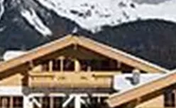 Ein wunderschönes Chalet im Schnee mit beeindruckenden Bergen im Hintergrund. Die klare, blaue Himmel sorgt für eine malerische alpine Kulisse.