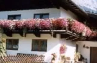 A charming house with a balcony full of flowers. In the background, the mountains are visible and the sky is clear.
