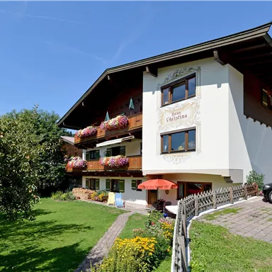 Ein malerisches Haus im alpinen Stil umgeben von Grün. Es bietet Balkone mit Blumen und einen gepflegten Garten.