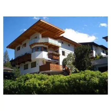 Ein modernes Haus mit Holzbalkon und grünem Garten. Der Himmel ist klar und blau.