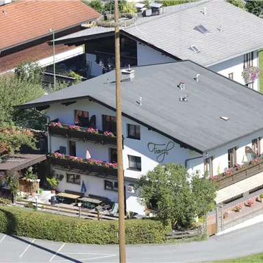 A cozy house with a shingle roof and blooming balconies. Surrounded by green trees and a well-maintained garden.