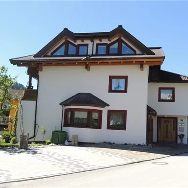 Ein modernes Haus mit einem einstöckigen Design und einem Satteldach. Der Vorgarten ist gepflegt und von Bäumen umgeben.