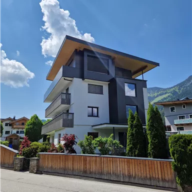 A modern building with multiple floors and large windows. Surrounded by trees and a quiet street.
