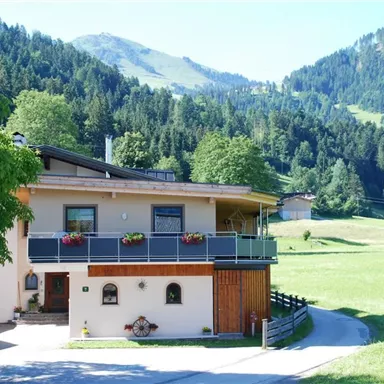 Ein schönes Haus in einer grünen Landschaft mit Bergen im Hintergrund. Die Umgebung ist freundlich und einladend.