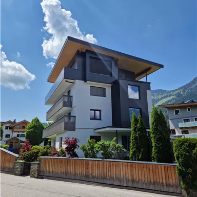 Ein modernes Haus mit einem einzigartigen architektonischen Design. Die Umgebung ist grün mit Bäumen und anderen Gebäuden in der Nähe.