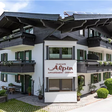 A charming house in alpine style with balconies and green plants. It is located on a quiet street in a picturesque setting.