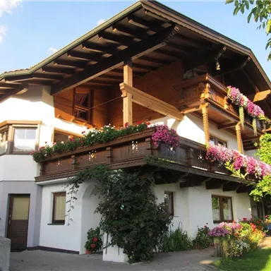 Ein charmantes Haus im alpinen Stil mit einem Balkon voller Blumen. Es ist von grünen Pflanzen umgeben und strahlt eine gemütliche Atmosphäre aus.