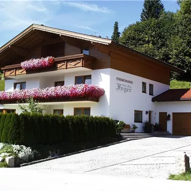 Ein charmantes Ferienhaus mit Balkonen voller Blumen. Die Umgebung ist grün und von Bäumen umgeben.