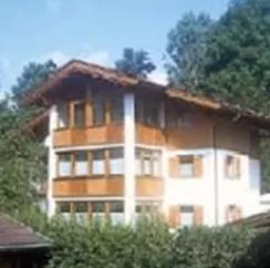 An Austrian house with wooden cladding and large windows. Surrounded by a green garden and trees.