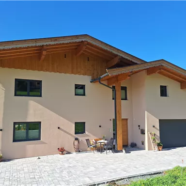 Ein modernes Haus mit Holzdetails und großen Fenstern. Der Außenbereich ist gepflastert und bietet einen Platz zum Entspannen.