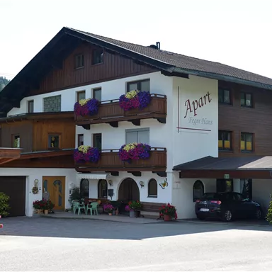 Ein charmantes Gebäude mit mehreren Etagen und Balkonen, geschmückt mit Blumen. Im Hintergrund sind Wald und Berge zu sehen.