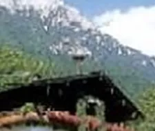 Eine schöne Almhütte umgeben von grünen Wiesen und majestätischen Bergen. Der Himmel ist blau mit wenigen Wolken.