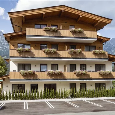 Ein modernes Gebäude mit Holzelementen und Blumenkästen. Im Hintergrund sind beeindruckende Berge sichtbar.