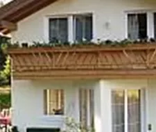 A beautiful house with a balcony and a well-maintained garden area. In the background, mountains and trees are visible.