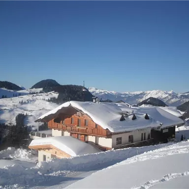 Ein malerisches Haus im Schnee, umgeben von schneebedeckten Bergen. Der Himmel ist klar und blau.