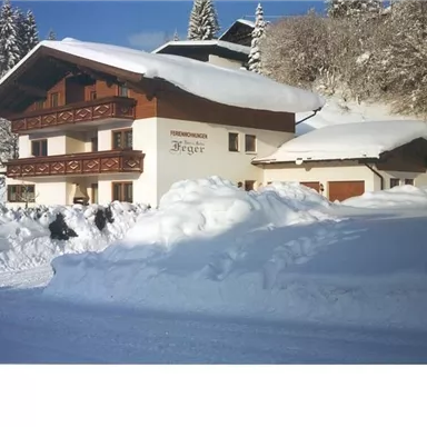 Ein gemütliches Chalet im Schnee, umgeben von verschneiten Bäumen. Der Himmel ist klar und die Landschaft wirkt winterlich und idyllisch.