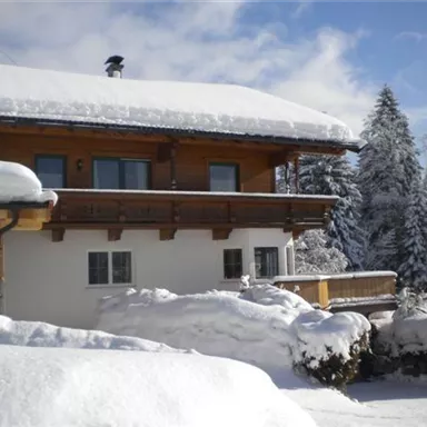 A cozy house in the snow with a wooden balcony. All around, the landscape is surrounded by snow-covered trees.