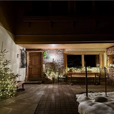 Ein wunderschöner Eingangsbereich mit einem geschmückten Weihnachtsbaum und festlicher Beleuchtung. Die schneebedeckte Umgebung verleiht der Szene eine gemütliche Atmosphäre.