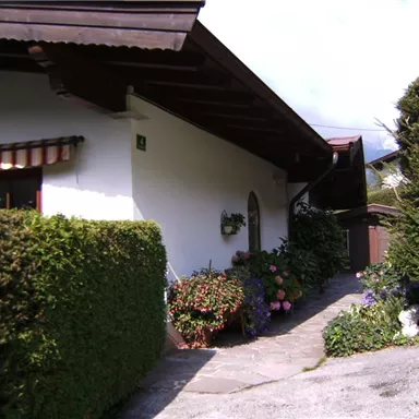 Ein charmantes Haus mit einem gepflegten Garten und bunten Blumen. Der Weg zum Eingang ist von hohen Hecken gesäumt.