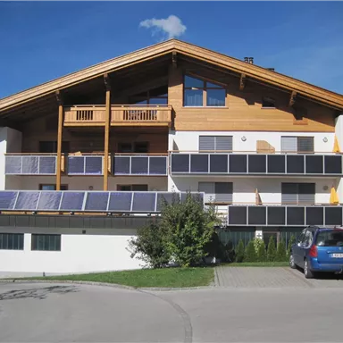 A modern building with wood details and several balconies. There are solar panels on the roof and a parking space in front of the house.