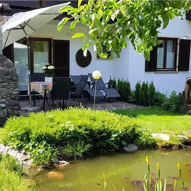 A beautiful garden with a pond and a terrace. The surroundings are green and inviting, perfect for relaxing.
