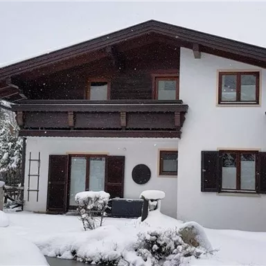 Ein weißes Haus im Schnee mit einem Dach in Holzoptik. Der Garten ist winterlich verschneit und ruhig.