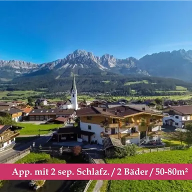 Eine malerische Alpenlandschaft mit Blick auf Berge und grüne Wiesen. Im Vordergrund sind gemütliche Häuser und eine Kirche zu sehen.