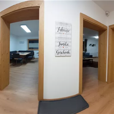 A bright room with several doors and a wooden floor. A decorative sign with positive sayings hangs on the wall.