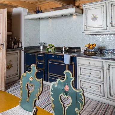 A cozy kitchen with a blue-painted stove and wooden cabinets. The room is bright and has decorative elements like fruits and stylish chairs.