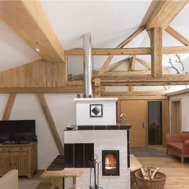 A cozy living room with a wooden ceiling and a modern fireplace. Bright, inviting furniture creates a warm atmosphere.