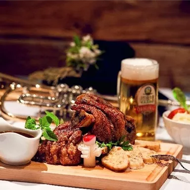 Ein köstliches Gericht mit perfekt geröstetem Fleisch auf einem Holzbrett. Dazu gibt es Bier, Soße, Brot und frische Beilagen.