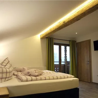 A cozy bedroom with a double bed and modern wooden furniture. Large windows with green curtains provide plenty of daylight.