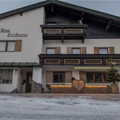 A charming building named "Haus Landmann". It features alpine architecture and is surrounded by snow.
