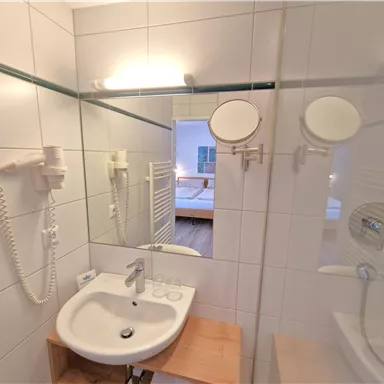 Ein modernes Badezimmer mit einem Waschbecken und einem großen Spiegel. Die Wände sind hell gefliest und es gibt einen Haartrockner.