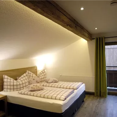 A cozy bedroom with a double bed and pillows. Large windows let in light and provide access to a balcony.